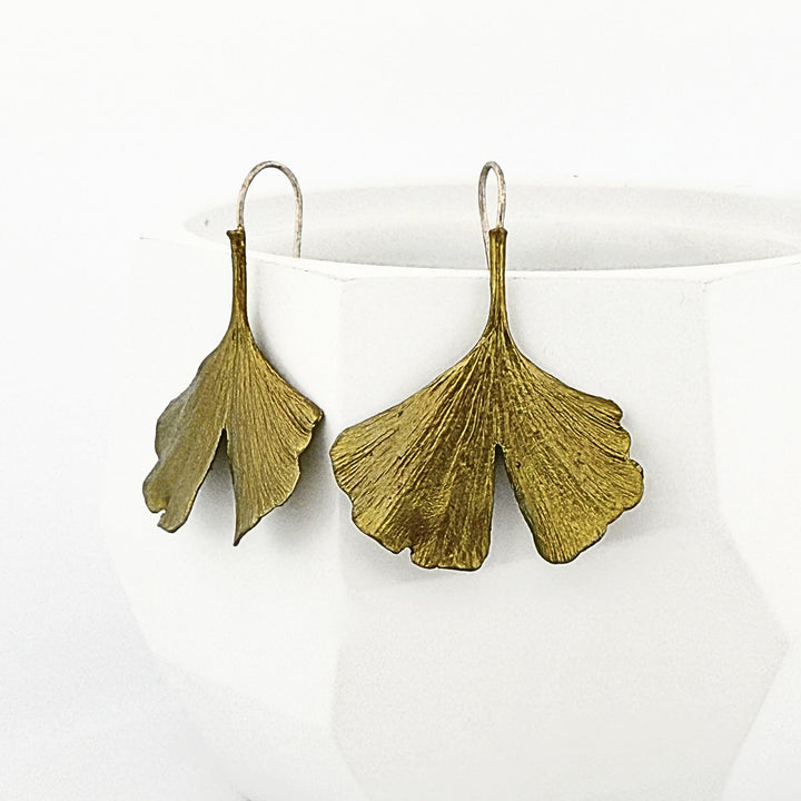 Gold leaf-shaped earrings on a white surface