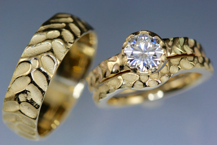 Full image of matching set of cobblestone engagement ring, wedding band, and men's wedding band all next to one another.