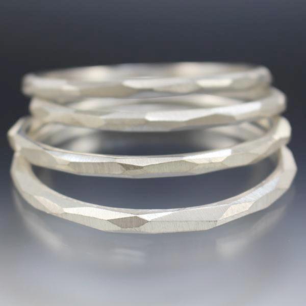 A stack of sterling silver bangle bracelets that have a faceted texture.