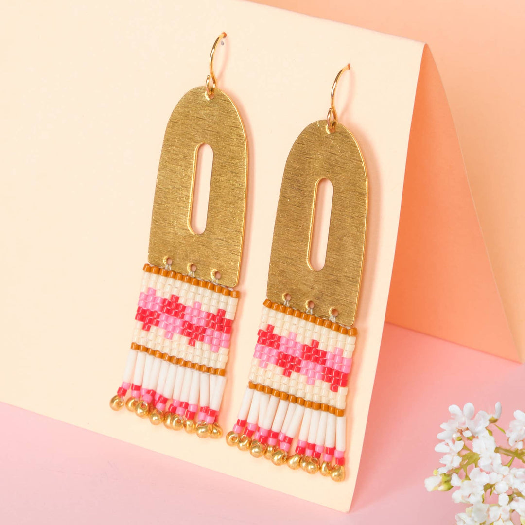 Gold earrings with pink and white beaded details on a pink background