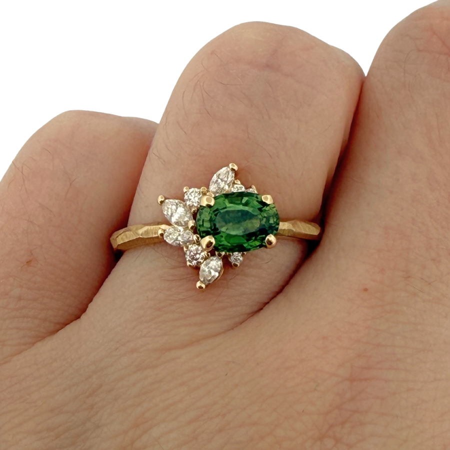 Gold ring with a green gemstone and diamonds on a finger against a white background