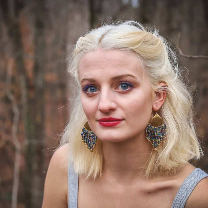 Woman with blonde hair and blue eyes wearing large earrings in a forest setting