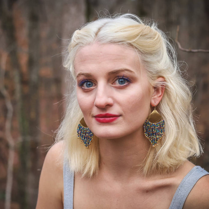 Woman with blonde hair and blue eyes wearing large earrings in a forest setting