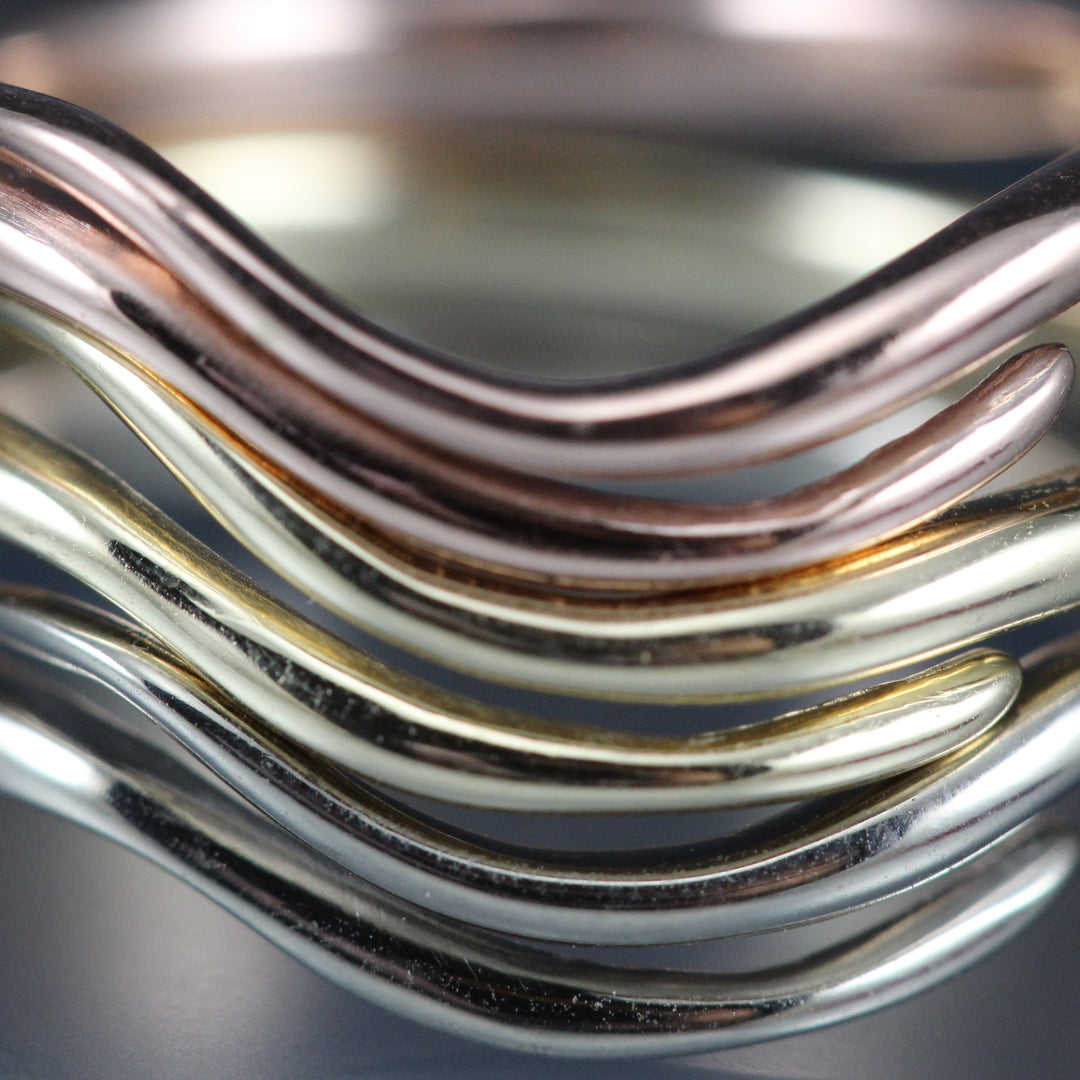 A detail photograph of three rings stacked together, rose, yellow and white gold.