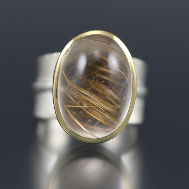 Full image of Golden Rutilated Quartz Ridge Ring. The rutilated quartz is in the shape of an oval, encompassed in gold and placed on a chunky silver band.