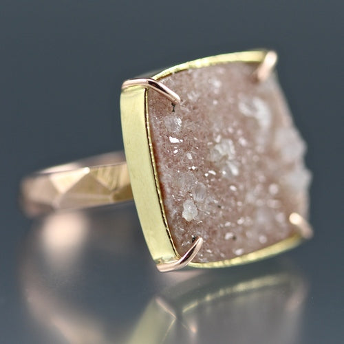 Angled view of Peach Druzy Chiseled Ring #3. The peach druzy is cut in the shape of a square, set with a gold border and four rose gold prongs, on a rose gold chiseled band.