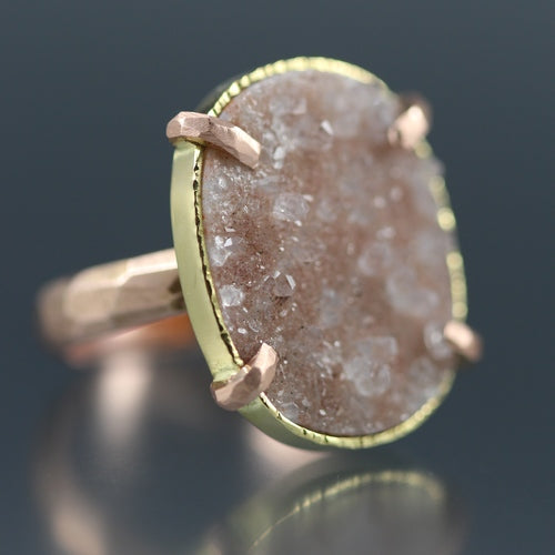 Angled view of Peach Druzy Chiseled Ring #2. The peach druzy is cut in an oval, set in gold with four rose gold prongs, laying on a rose gold chiseled band.