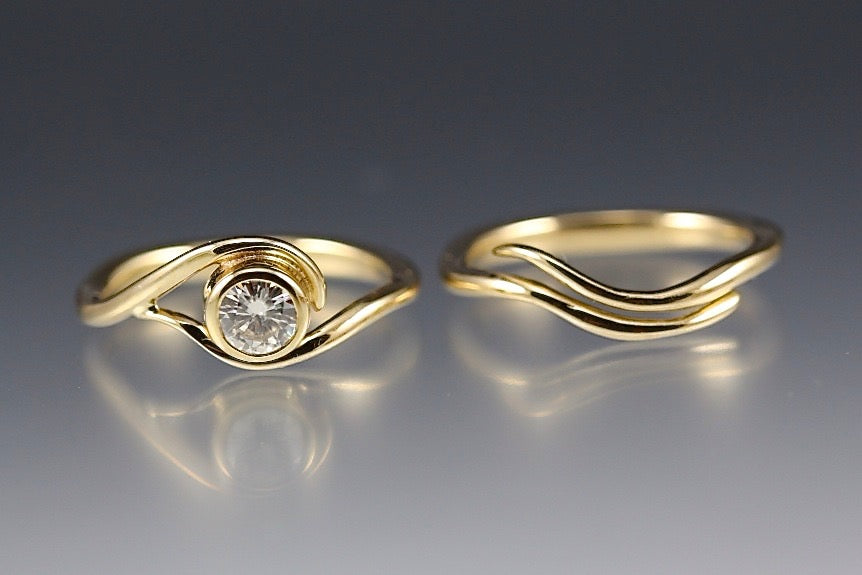 Yellow Gold and Moissanite Engagement ring and nesting wedding band that have a vine or wave appearance.