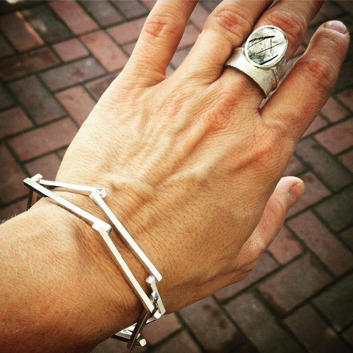 A woman's wrist and hand wearing a stack of silver bangle bracelets and a large silver ring.