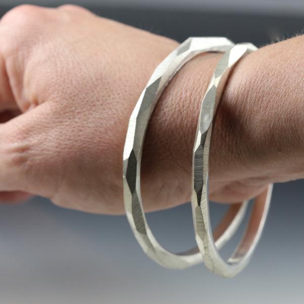 A woman's wrist wearing two sterling silver bangle bracelets that have a faceted texture.