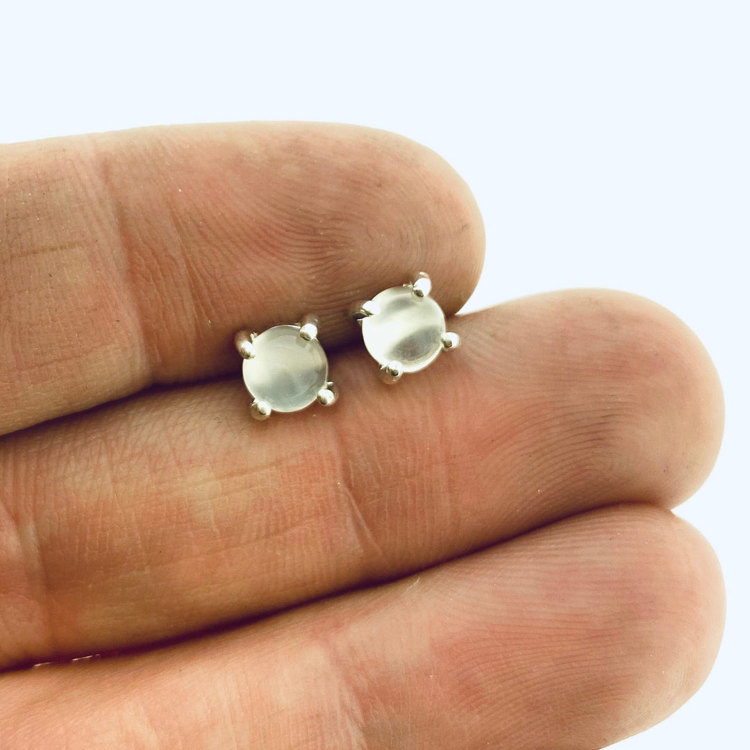 Full view of clear small round cabochon stud earrings in-between two fingers to help give idea of scale of piece.