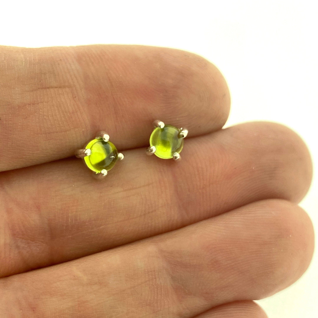 Full view of yellow/green small round cabochon stud earrings in-between two fingers to help give idea of scale of piece.