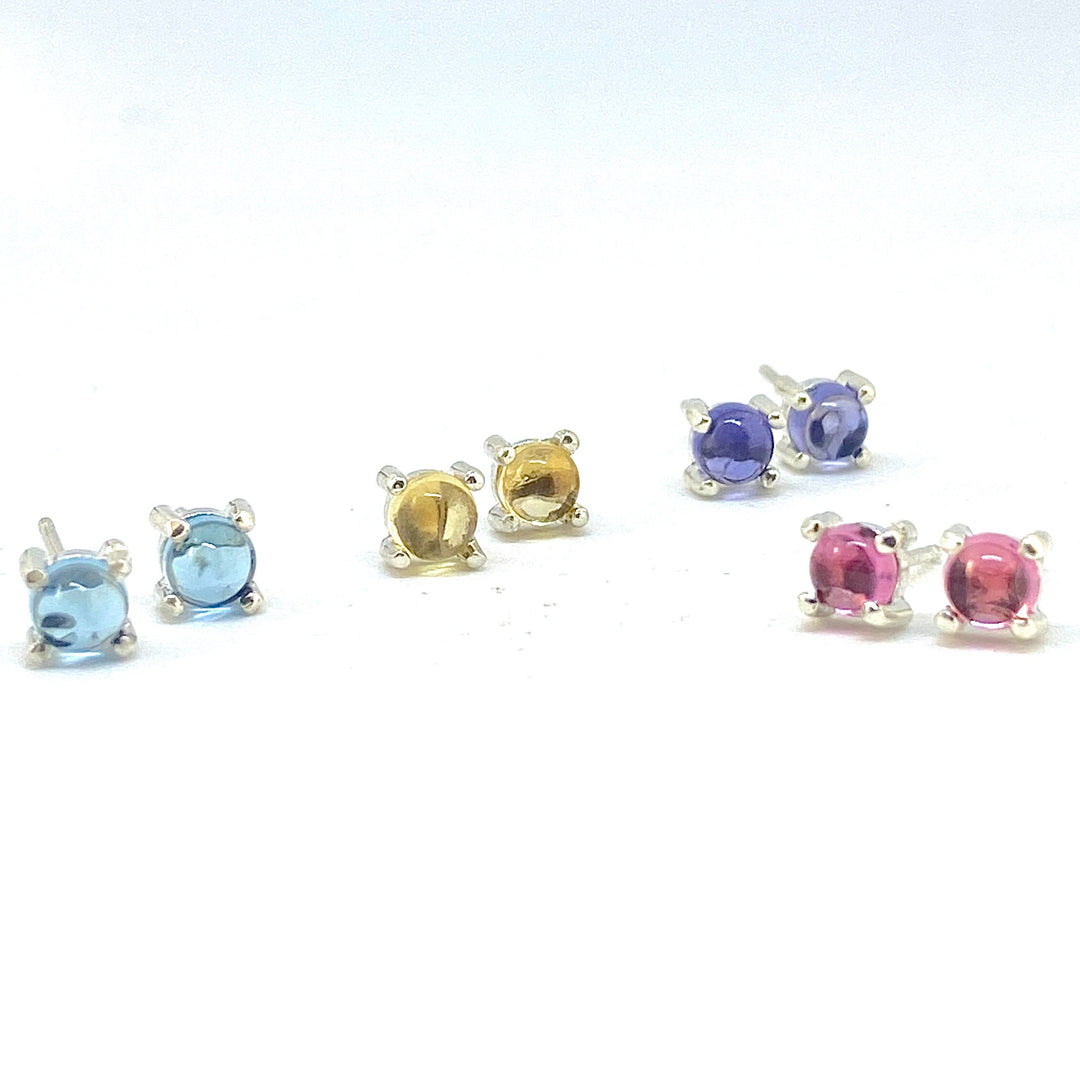 Full view of four different colored (light blue, yellow, navy blue and pink) tony round cabochon stud earrings all set in silver with four prongs.