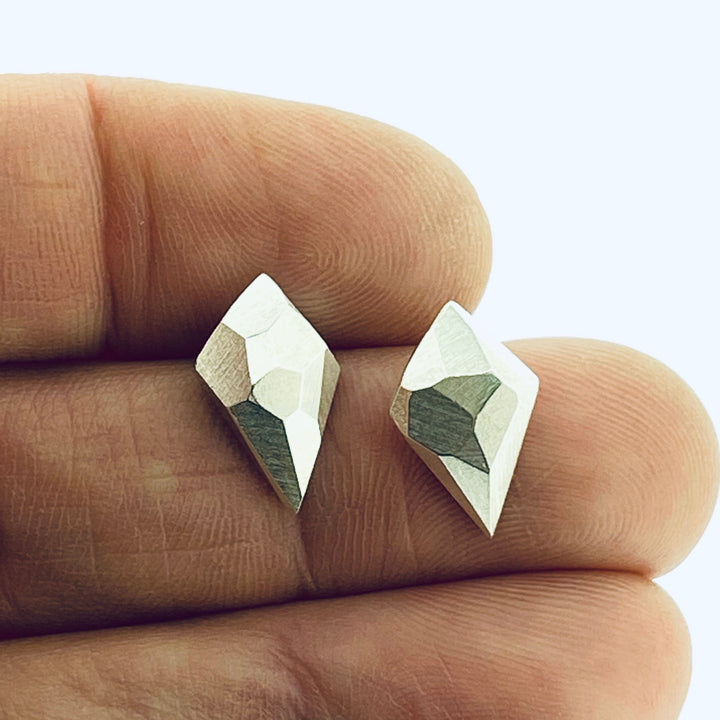 Full view of diamond faceted stud earrings in-between two fingers to give idea of scale.