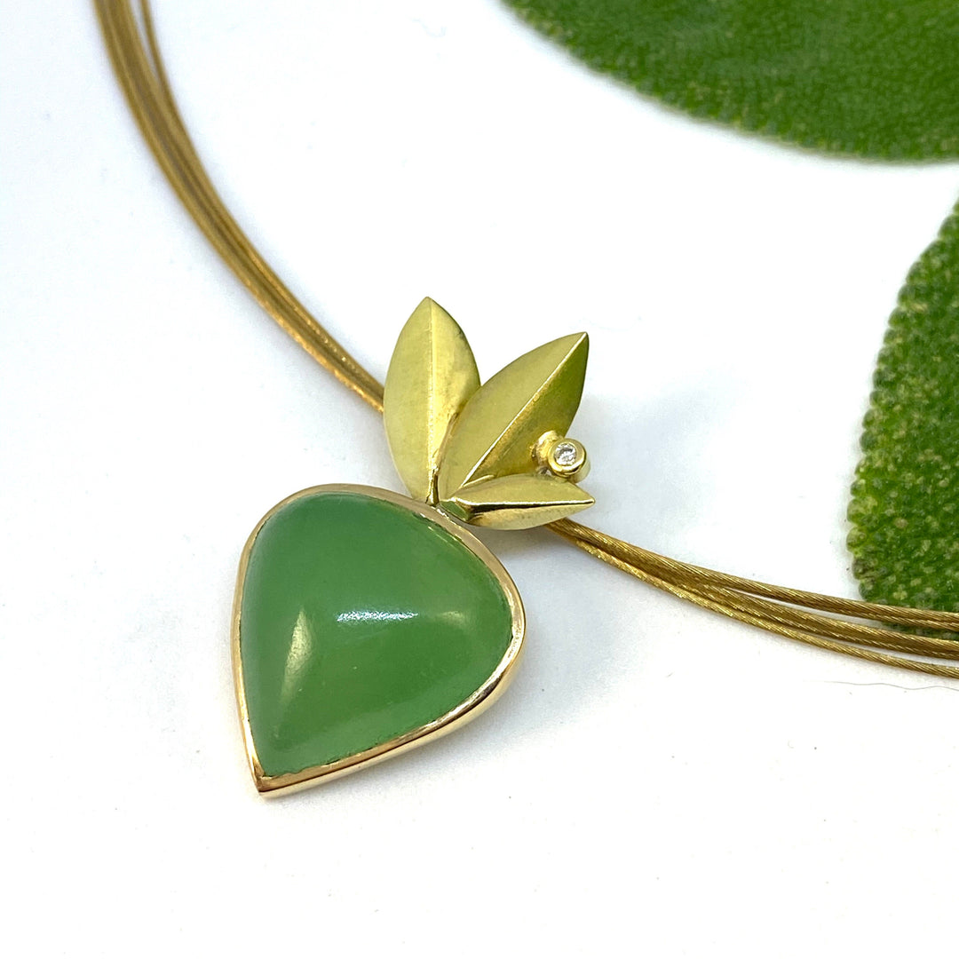 Full image of pendant on Chrysoprase - Bloom Pendant. This pendant is in the shape of an upside-down acorn encompassed in gold. The top has three gold leaves with a set diamond in-between the middle and right leaf. This pendant is on multiple string of gold band as the chain for the necklace.