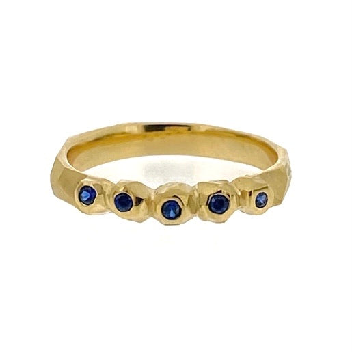 Full image of Multiple Nugget Facet Ring on its side. This ring is made of gold and has five set blue sapphires on its band. The settings of the sapphires are cut and sanded around that look like a nugget of gold enveloping the sapphires.