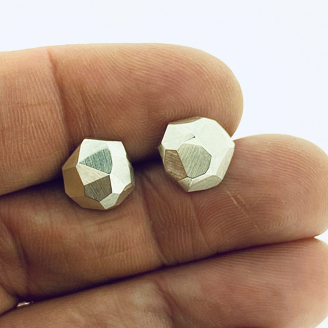 Full view of faceted stud earrings in-between two fingers to give idea of scale of piece. 