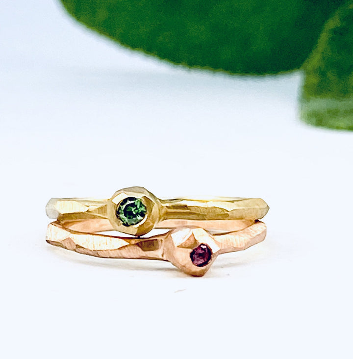 Full image of two Nugget Facet Rings stacked on top of one another. The top is made of yellow gold and has a set green diamond that has the gold enveloping it to look like a nugget. The bottom has a set pink sapphire. Both are on a chiseled textured band.