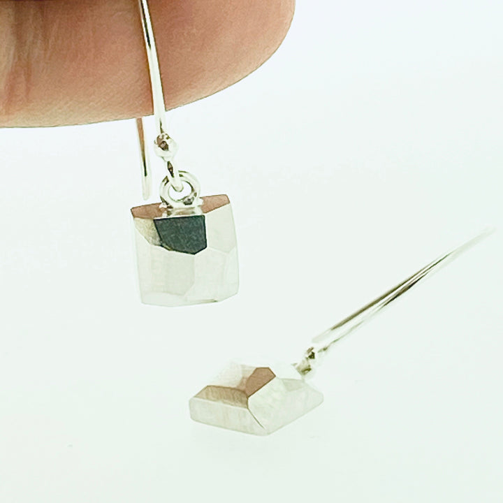 Full view of square faceted dangle earrings. One is laying down while the other is laying on top of a finger to give idea of scale.