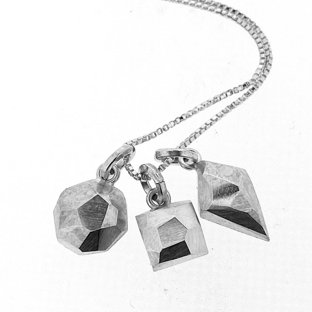 Full view of Faceted Dainty pendant. These three pendants are all made of silver and resemble an octagon, square and diamond all with a faceted texture.