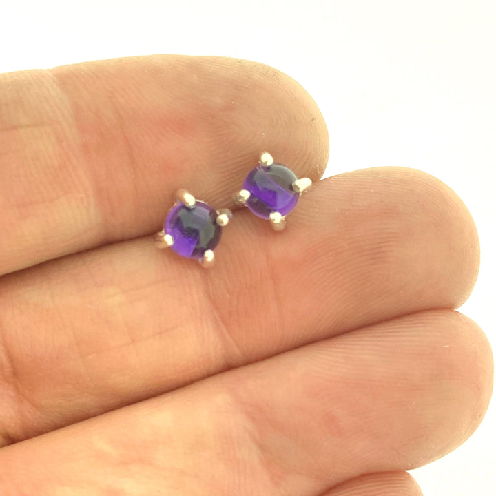 Full view of navy blue small round cabochon stud earrings in-between two fingers to help give idea of scale of piece.
