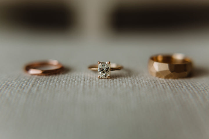 Full view of Radiant Cut Moissanite - Chiseled Engagement Ring with two chiseled wedding bands next to it. To the left of the engagement ring is the woman's more slender wedding band and to the right is the man's chunkier wedding band.
